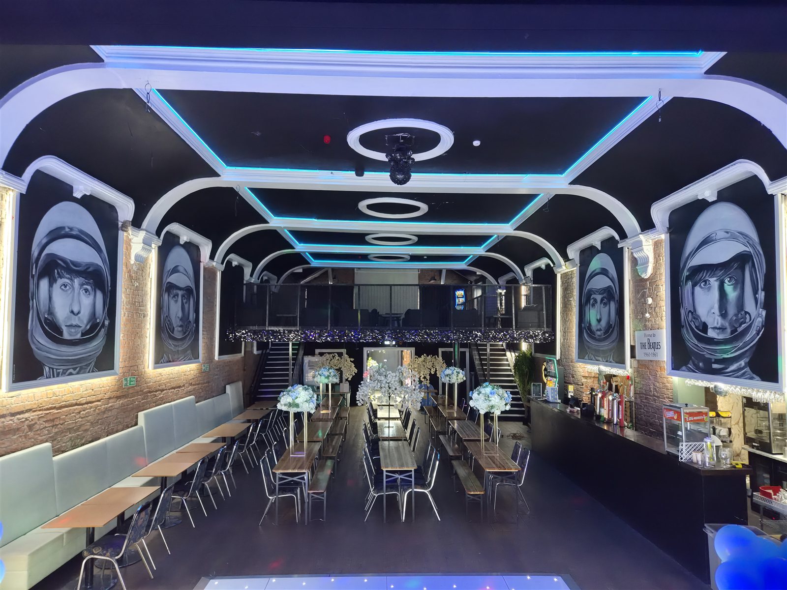 The full hall with blue ceiling lighting, Beatles portraits, seating and floral decorations.