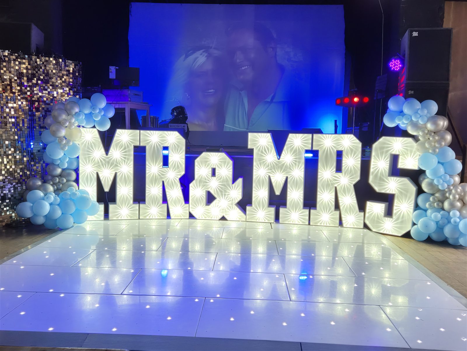 Wedding celebration setup with light-up letters and a projection screen.
